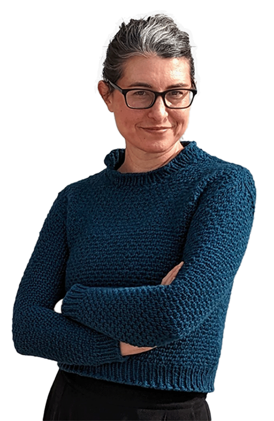 This is an image of me! I'm a white femme human in my 40s with a slight streak of gray in my dark hair. My arms are folded in front of me and I've got a self-satisfied look on my face as I sort of lean against a white brick wall. I'm wearing a blue sweater I knitted myself, black pants, and black and gold high top converse.